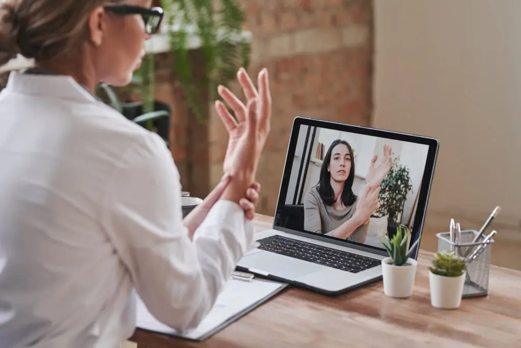 A person video chatting on a laptop while gesturing with their hand.